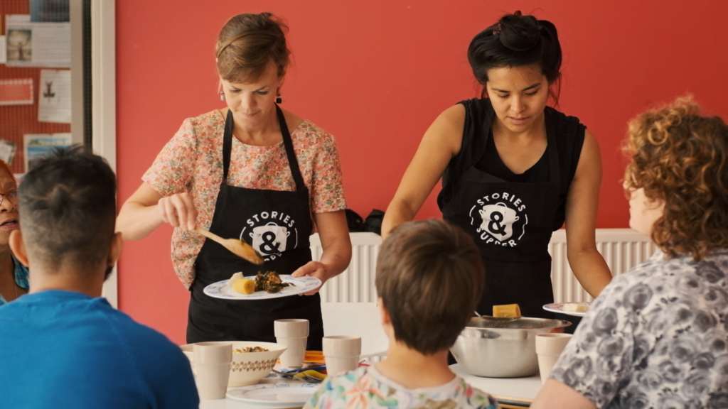 Two women happily serving food to three other people