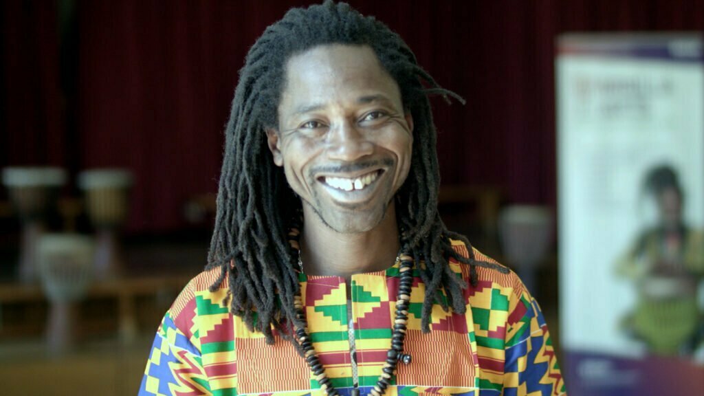 A portrait of a man wearing colourful clothes and smiling happily at the camera