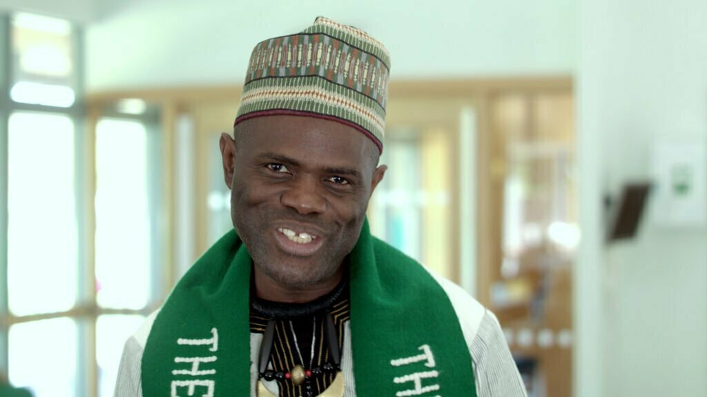 A portrait of a man wearing a green neck piece smiling at the camera